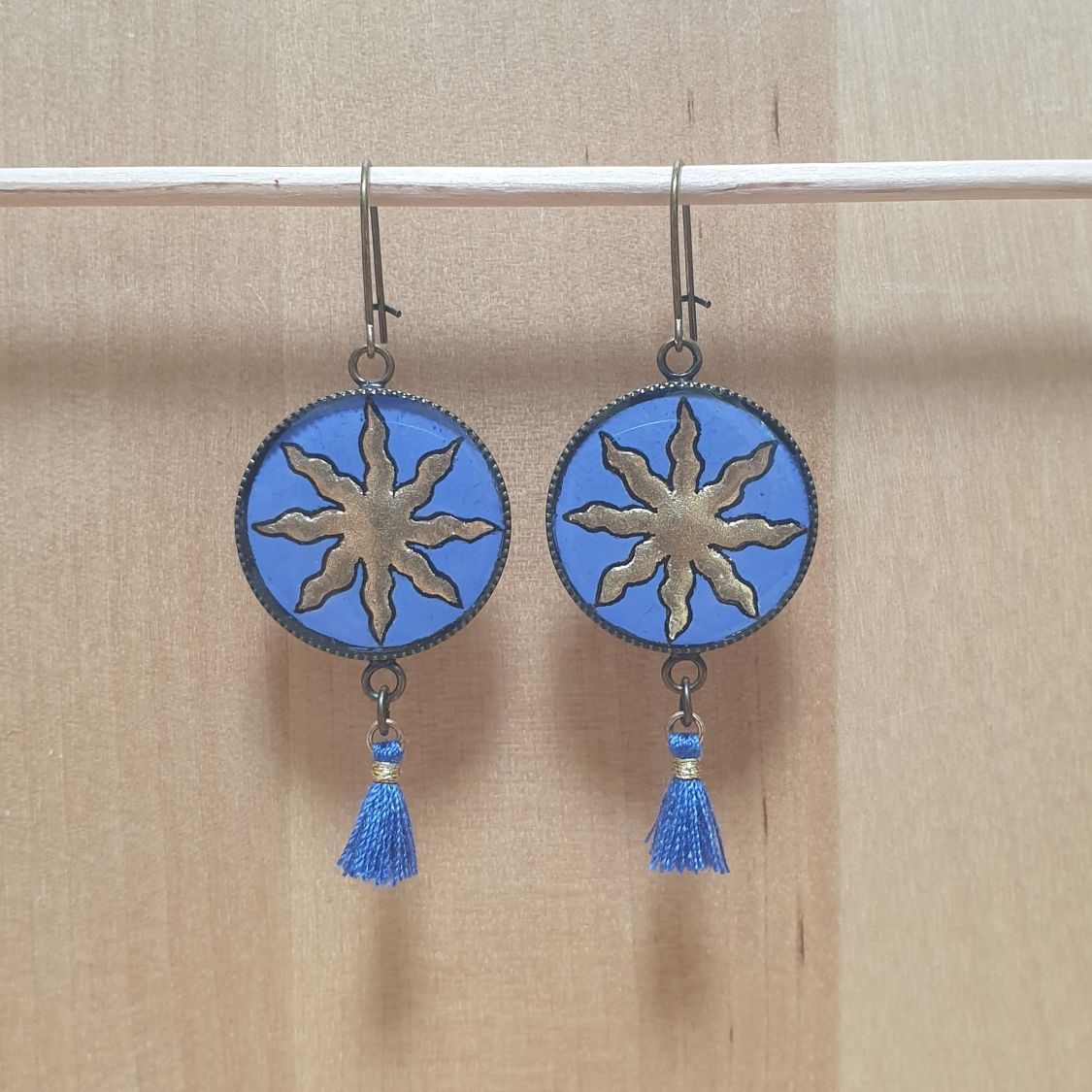 Boucles d'oreille pendantes soleil dorée sur fond bleu