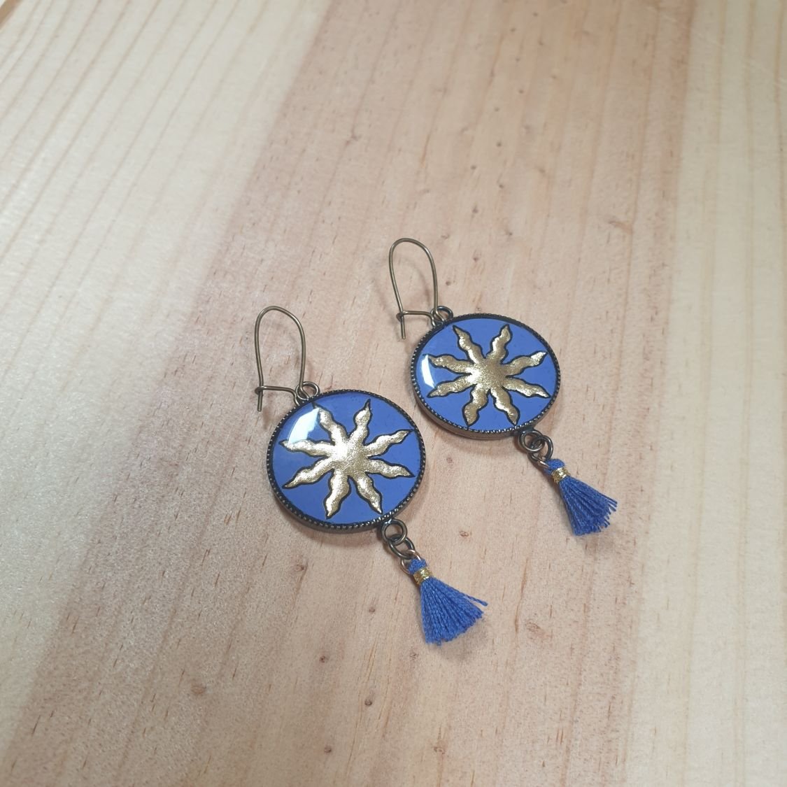 Boucles d'oreille pendantes soleil dorée sur fond bleu