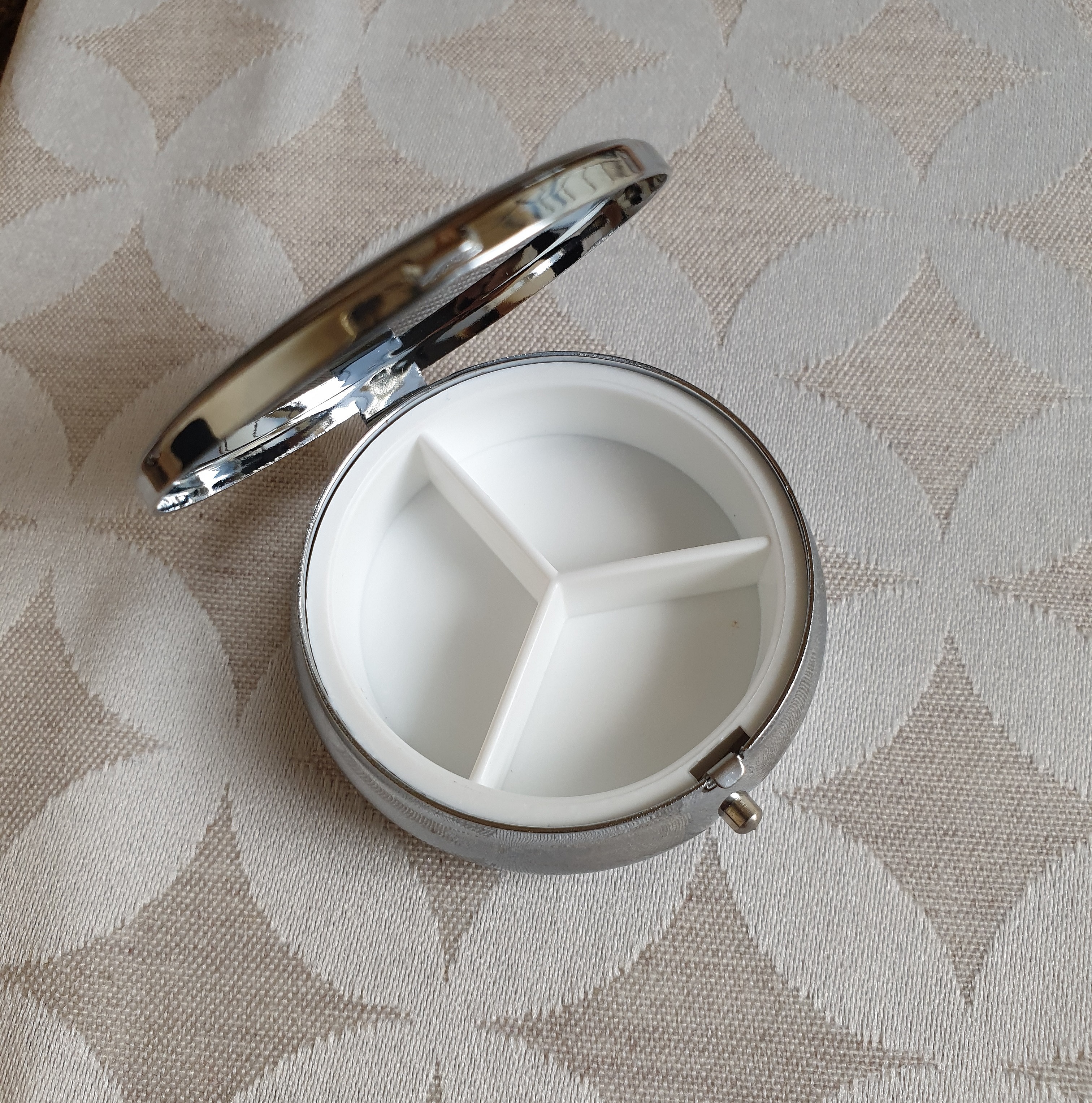 Petit pilulier métallique compartimenté avec couvercle ouvert.