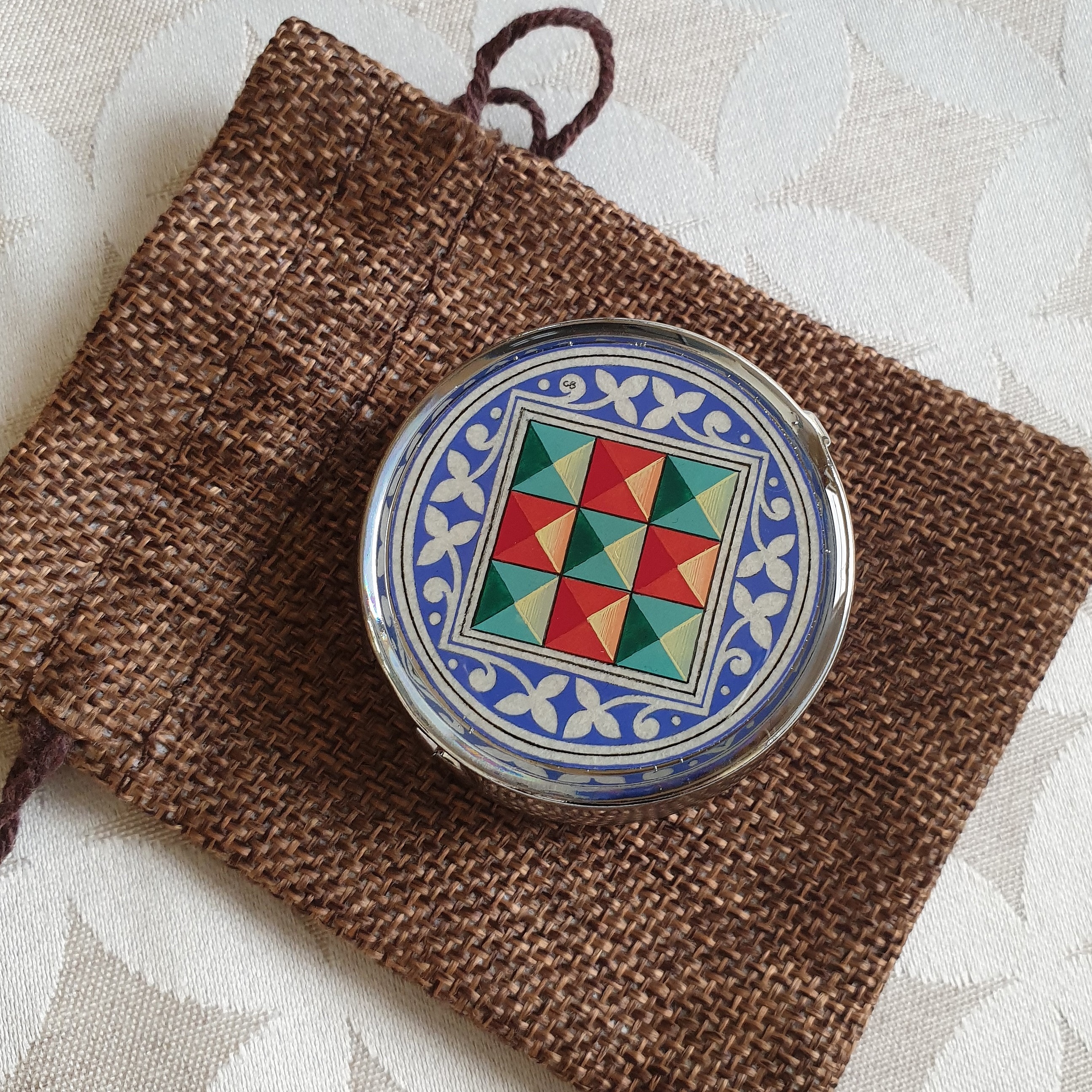 Petit pilulier métallique avec enluminure florentine sur pochon en toile.