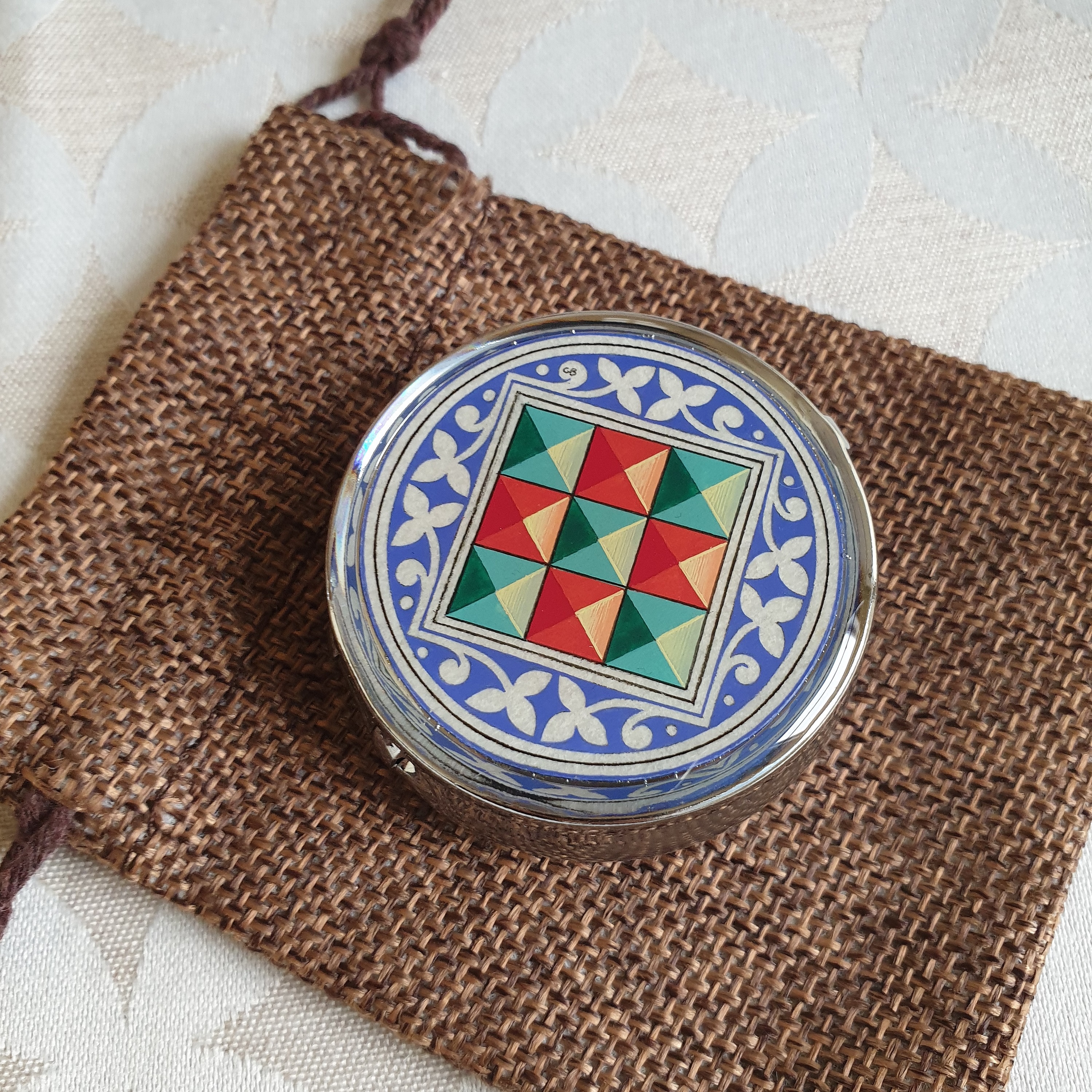 Petit pilulier métallique avec enluminure florentine sur pochon textile.