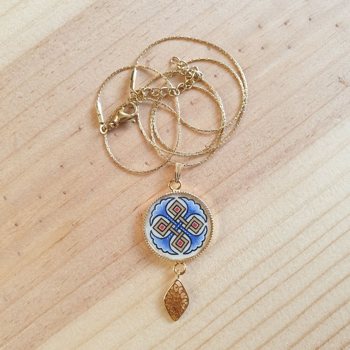 Collana con ciondolo illuminato da palmette blu, intrecci dorati e rossi su catena d'oro